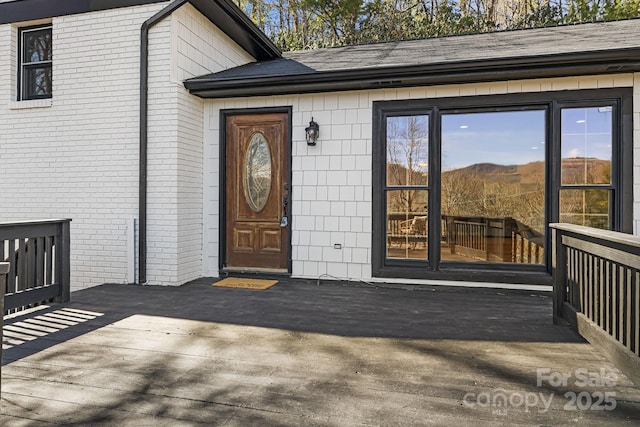 entrance to property featuring a deck and brick siding