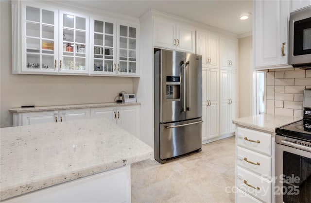 kitchen with light stone counters, stainless steel appliances, white cabinets, decorative backsplash, and glass insert cabinets