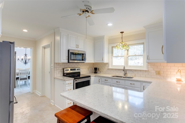 kitchen with light stone counters, appliances with stainless steel finishes, white cabinets, a sink, and a peninsula