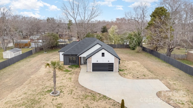 view of front facade with concrete driveway, board and batten siding, a garage, fence private yard, and a front lawn