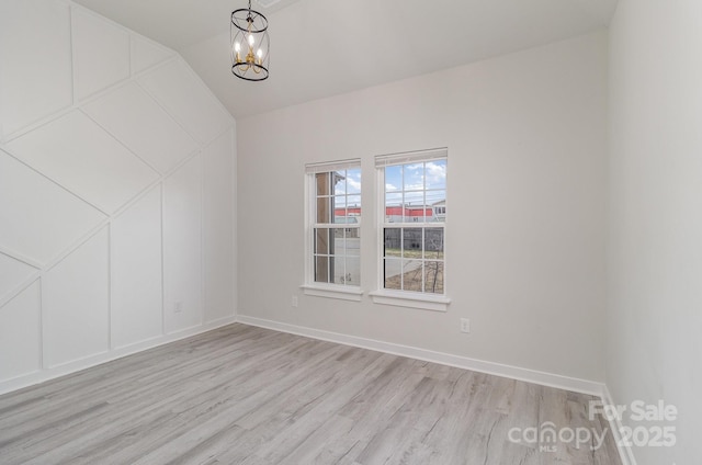 spare room featuring light wood-type flooring, a notable chandelier, a decorative wall, and baseboards