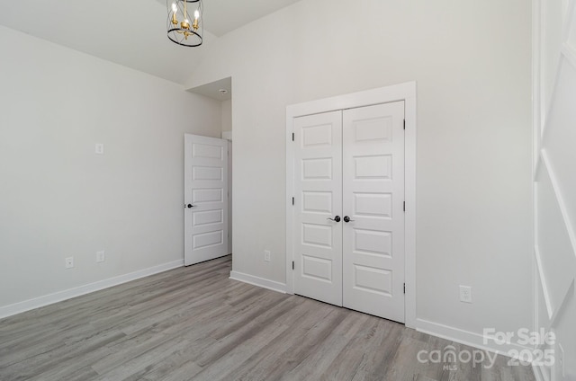 unfurnished bedroom with lofted ceiling, a notable chandelier, wood finished floors, baseboards, and a closet