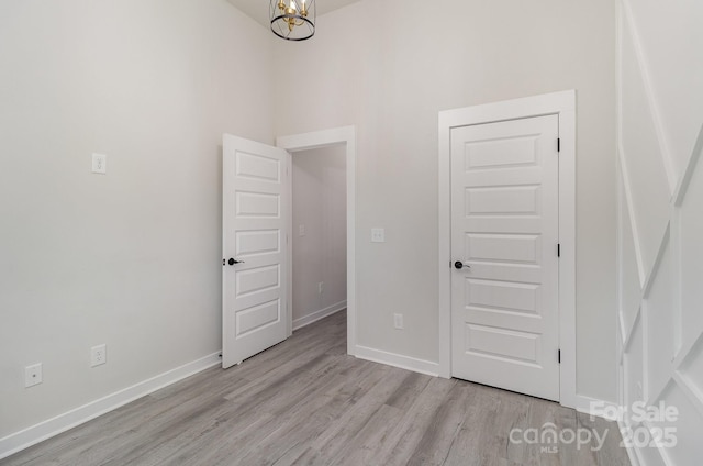 empty room with a high ceiling, an inviting chandelier, light wood-style flooring, and baseboards