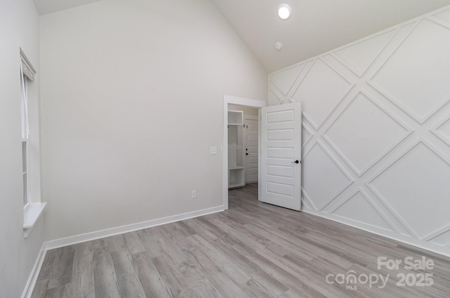 unfurnished bedroom with high vaulted ceiling, light wood-style flooring, and baseboards