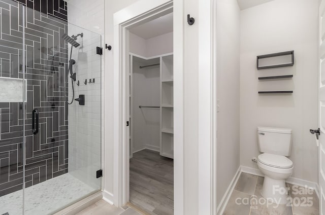 bathroom with toilet, a shower stall, a spacious closet, and wood finished floors