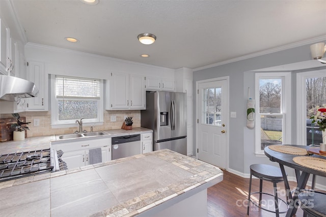 kitchen featuring tile counters, white cabinets, stainless steel appliances, under cabinet range hood, and a sink