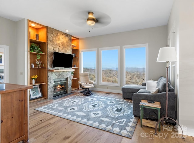 living area featuring a fireplace, wood finished floors, a ceiling fan, baseboards, and built in features