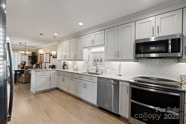 kitchen featuring stainless steel appliances, hanging light fixtures, ornamental molding, a sink, and a peninsula