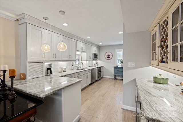 kitchen featuring decorative light fixtures, light wood finished floors, stainless steel appliances, glass insert cabinets, and a peninsula