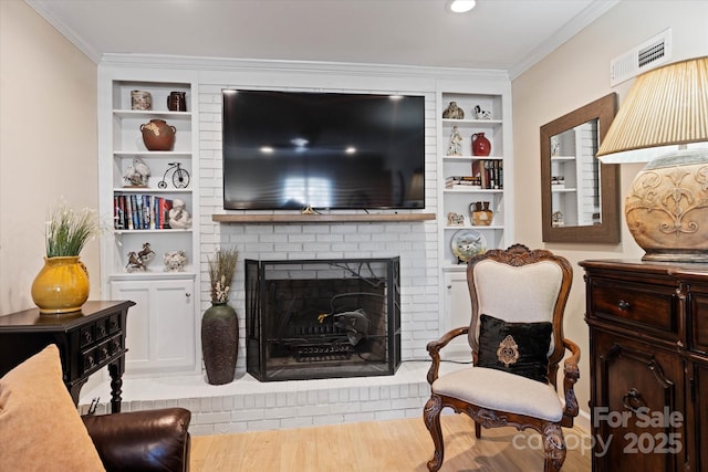 living area featuring built in shelves, visible vents, light wood-style flooring, ornamental molding, and a brick fireplace