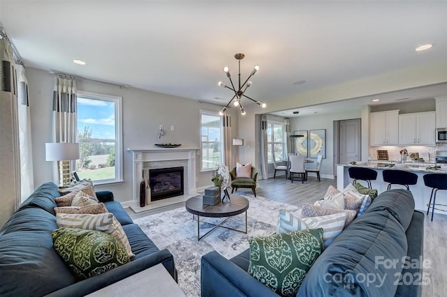 173 Glenn Dr, Mooresville, NC 28115 - living room featuring a chandelier, light wood-style flooring, baseboards, a glass covered fireplace, and recessed lighting