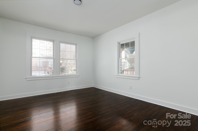 empty room featuring dark wood-style flooring, plenty of natural light, and baseboards