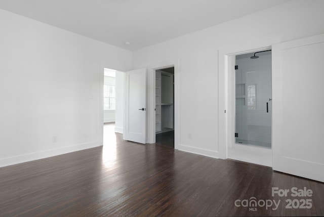 unfurnished bedroom featuring ensuite bathroom, dark wood-type flooring, a walk in closet, and baseboards