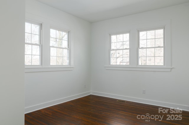 spare room with dark wood-type flooring, visible vents, and baseboards