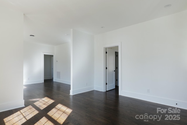 spare room featuring dark wood-type flooring, visible vents, and baseboards