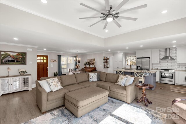 living area with light wood finished floors, ceiling fan with notable chandelier, ornamental molding, and recessed lighting