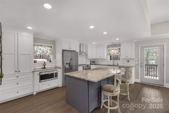 kitchen with wall chimney range hood, white cabinetry, stainless steel appliances, and a center island