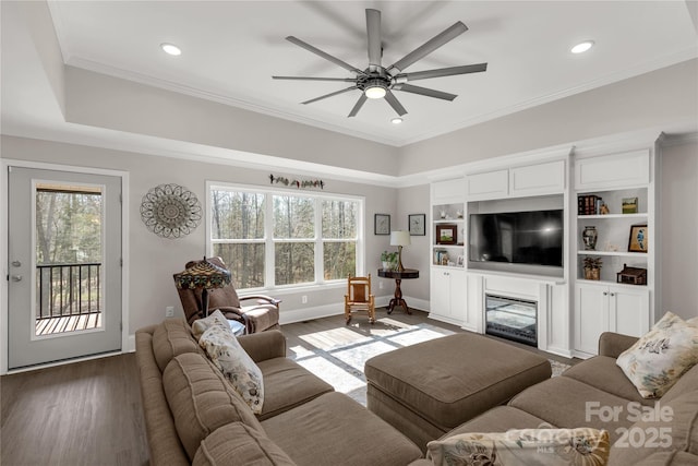 living area with ornamental molding, a glass covered fireplace, a ceiling fan, wood finished floors, and baseboards