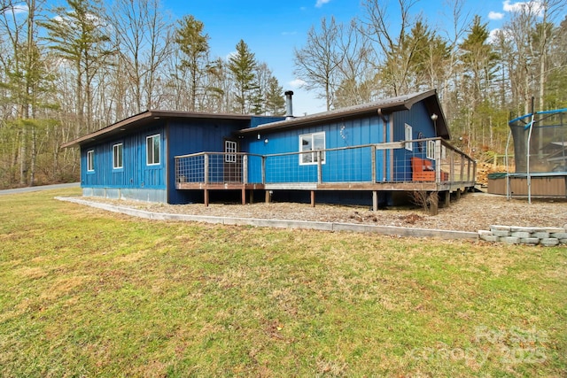 rear view of property featuring a trampoline, a deck, and a lawn