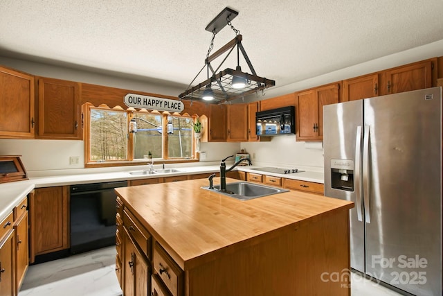 kitchen with an island with sink, decorative light fixtures, black appliances, wooden counters, and a sink