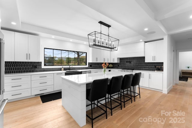 kitchen featuring light wood-style flooring, a tray ceiling, light countertops, and a sink