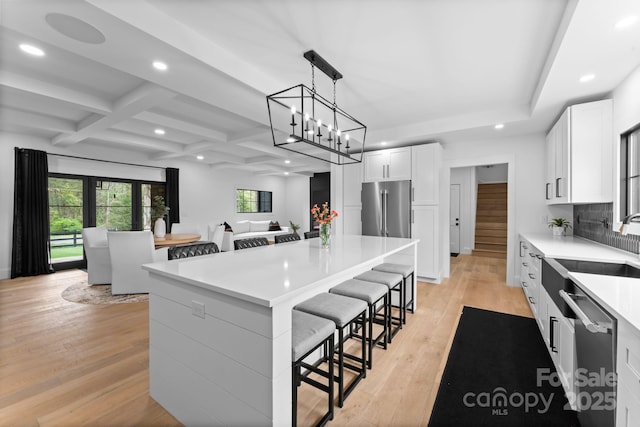 kitchen with appliances with stainless steel finishes, coffered ceiling, light wood-style floors, and a kitchen breakfast bar