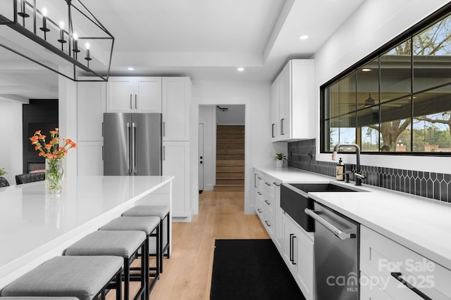 kitchen featuring a breakfast bar area, light countertops, appliances with stainless steel finishes, light wood-style floors, and white cabinetry