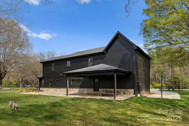 back of property featuring stone siding, roof with shingles, fence, a yard, and a patio area