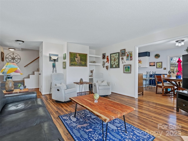 living area featuring a textured ceiling, wood finished floors, stairs, and baseboards