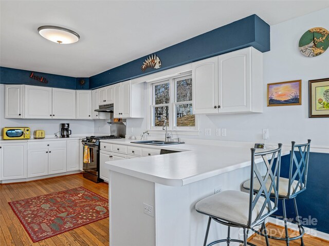 kitchen featuring light wood-style flooring, a breakfast bar, a peninsula, gas range oven, and a sink