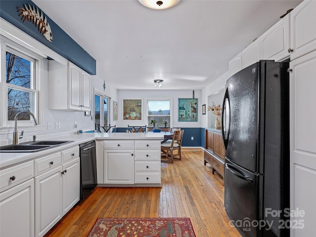 kitchen featuring a peninsula, black appliances, light wood-type flooring, and a sink