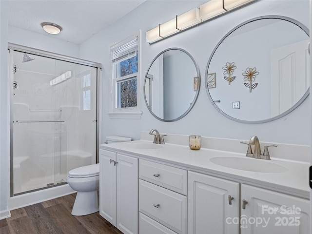 bathroom featuring double vanity, a sink, a shower stall, and wood finished floors