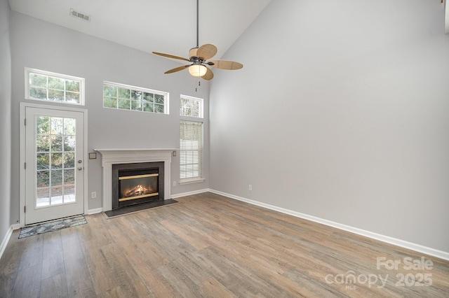 unfurnished living room with visible vents, light wood-style floors, a fireplace with flush hearth, high vaulted ceiling, and baseboards