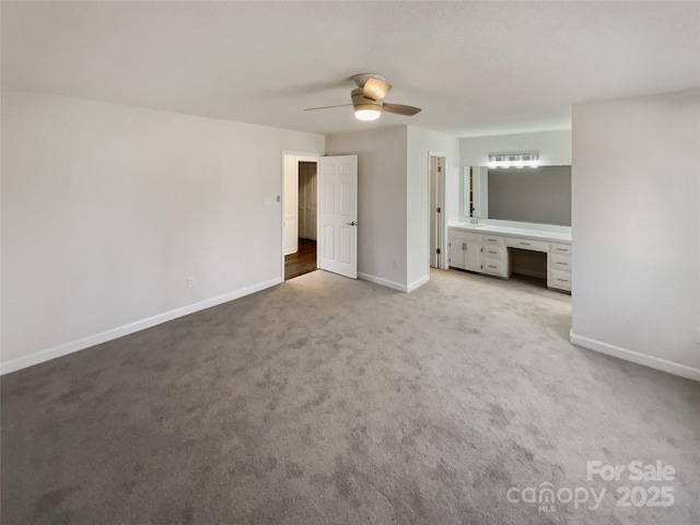 unfurnished bedroom featuring light carpet, baseboards, a ceiling fan, built in study area, and ensuite bathroom