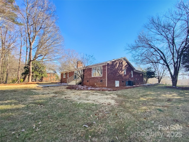 view of side of home featuring crawl space, brick siding, a chimney, and a yard