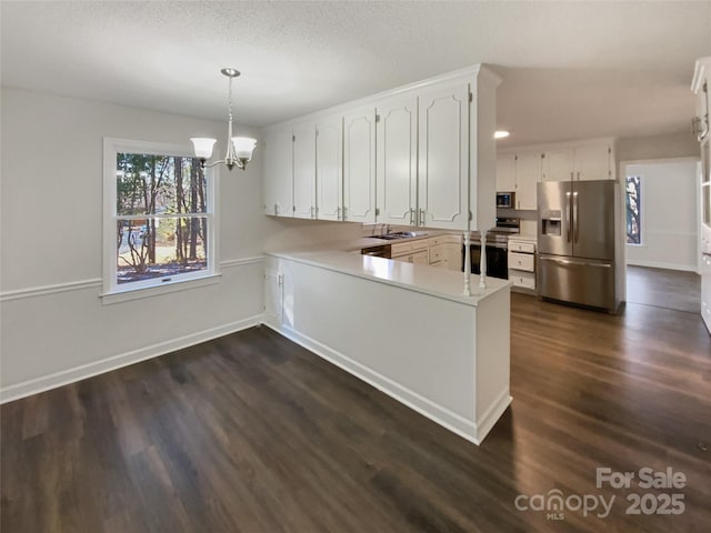 kitchen with stainless steel appliances, light countertops, hanging light fixtures, white cabinetry, and a peninsula