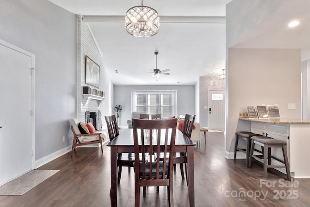 dining area with a brick fireplace, dark wood finished floors, baseboards, and ceiling fan with notable chandelier