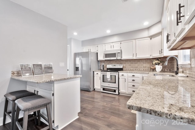 kitchen with light stone counters, a sink, white cabinetry, a kitchen breakfast bar, and appliances with stainless steel finishes