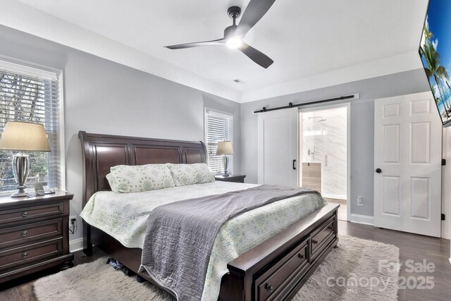 bedroom featuring ceiling fan, a barn door, dark wood-type flooring, visible vents, and baseboards