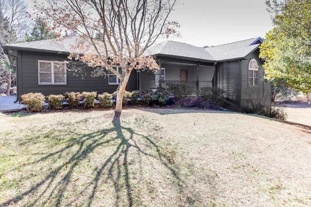 ranch-style house with covered porch, roof with shingles, and a front yard