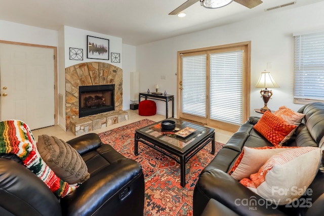 living room with ceiling fan, visible vents, and a stone fireplace