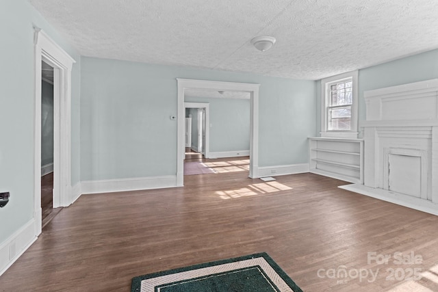 unfurnished living room featuring a textured ceiling, wood finished floors, and baseboards