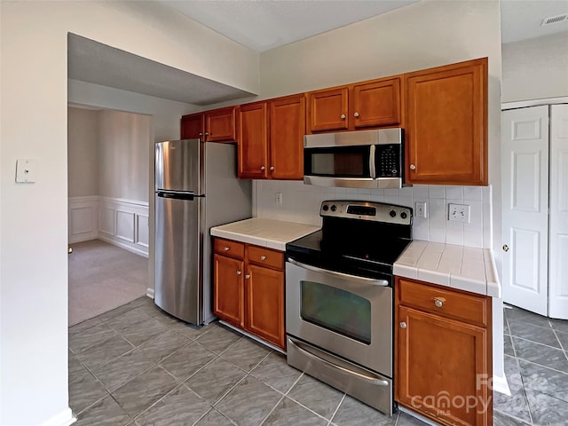 kitchen featuring brown cabinets, tasteful backsplash, visible vents, and stainless steel appliances