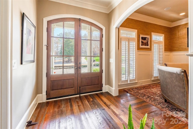 foyer with dark wood finished floors, arched walkways, french doors, wainscoting, and crown molding