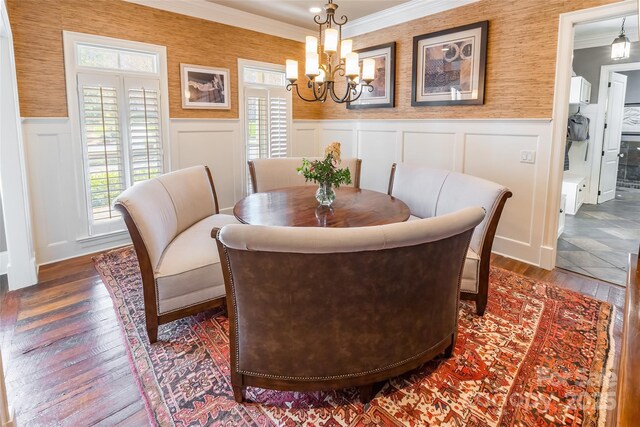 dining room featuring wallpapered walls, crown molding, hardwood / wood-style floors, wainscoting, and a notable chandelier