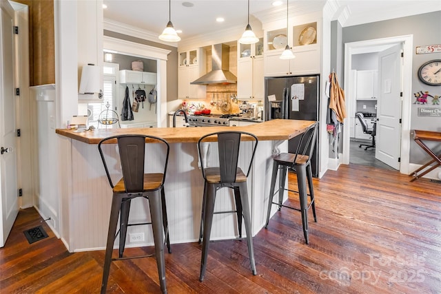 kitchen featuring wooden counters, glass insert cabinets, a kitchen breakfast bar, and wall chimney exhaust hood