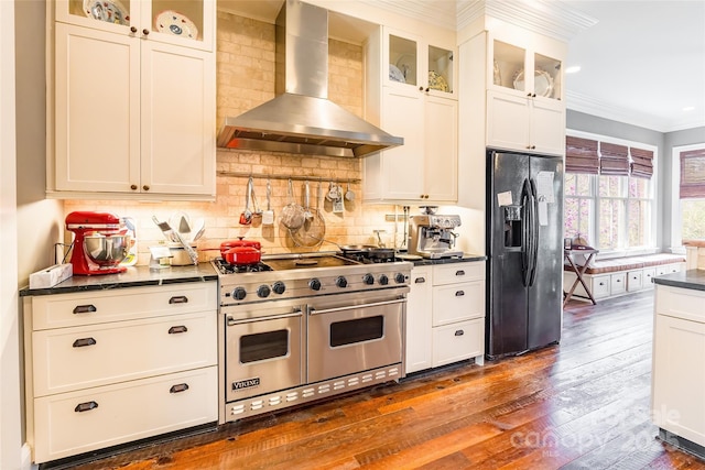 kitchen featuring double oven range, dark countertops, black fridge, and wall chimney range hood