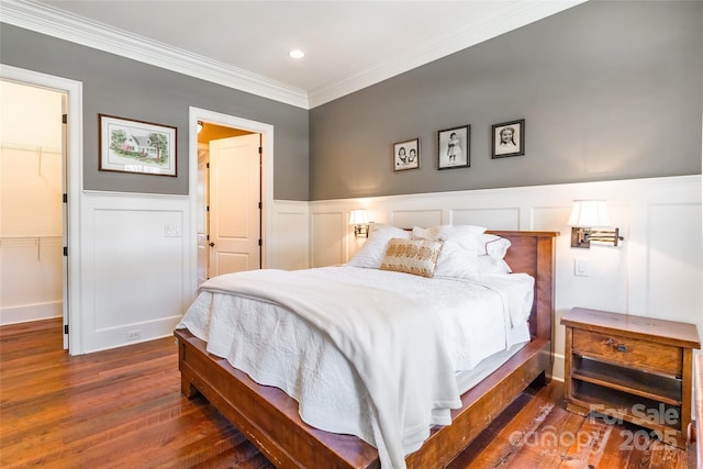 bedroom featuring a spacious closet, ornamental molding, recessed lighting, wainscoting, and wood finished floors