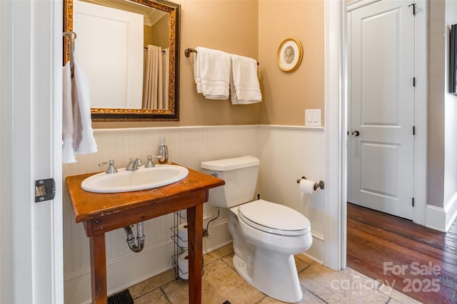 full bathroom featuring a sink, a wainscoted wall, and toilet