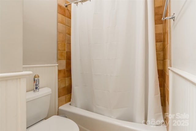 bathroom featuring a wainscoted wall, toilet, and shower / tub combo with curtain